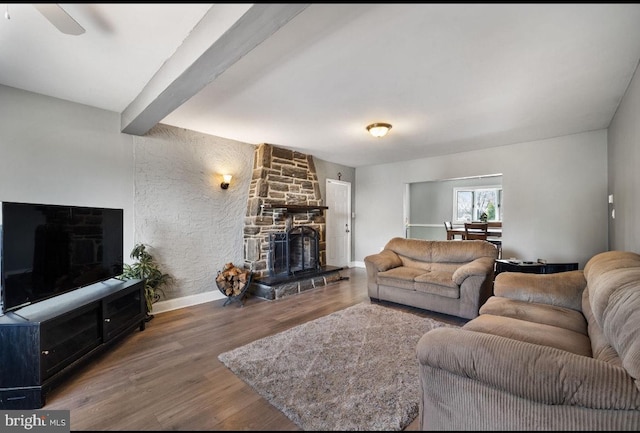 living area featuring a stone fireplace, beamed ceiling, wood finished floors, and baseboards