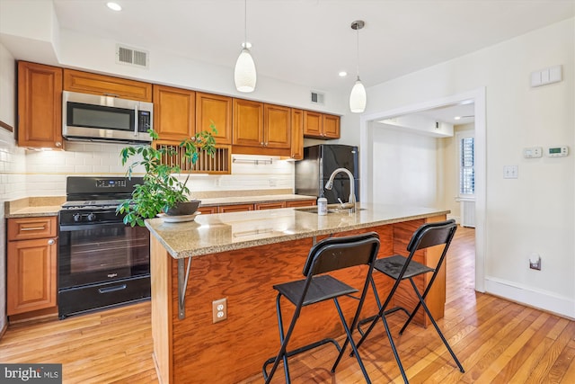 kitchen featuring visible vents, light wood-style flooring, a sink, black appliances, and backsplash