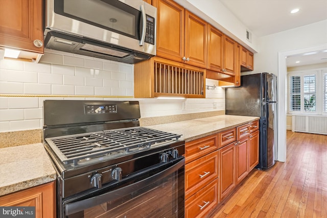 kitchen featuring brown cabinets, radiator, black appliances, and light stone countertops