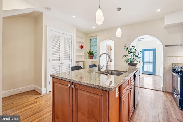 kitchen with dishwasher, brown cabinets, light wood-style flooring, black range with gas cooktop, and a sink