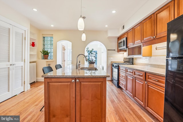 kitchen featuring light wood finished floors, radiator, black appliances, and a sink