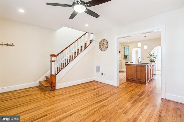 unfurnished living room featuring light wood finished floors, visible vents, baseboards, stairway, and a sink