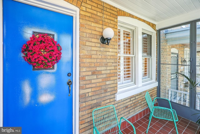 doorway to property with covered porch and brick siding