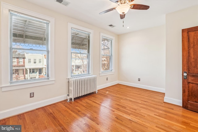 spare room featuring visible vents, a ceiling fan, radiator heating unit, light wood-style floors, and baseboards