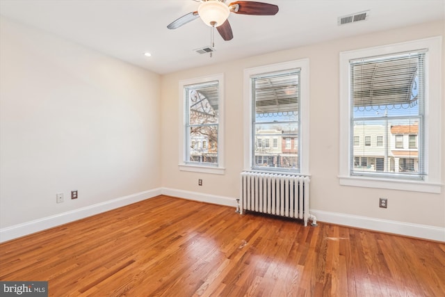 unfurnished room with visible vents, light wood-style flooring, radiator heating unit, and baseboards