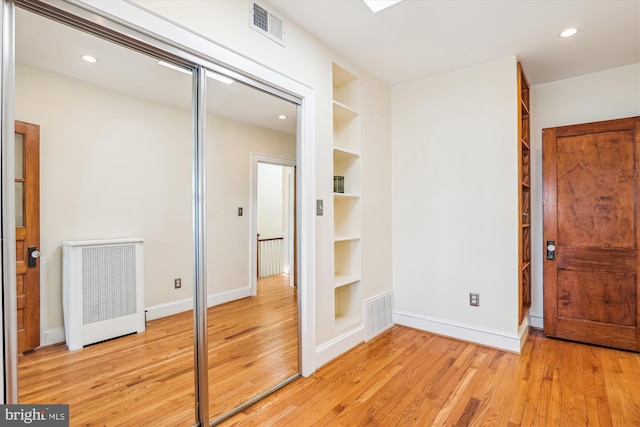 unfurnished bedroom featuring light wood-type flooring, visible vents, baseboards, and radiator