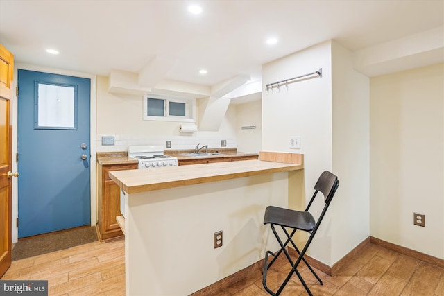 kitchen featuring light wood-style flooring, a kitchen breakfast bar, electric range, wood counters, and a sink