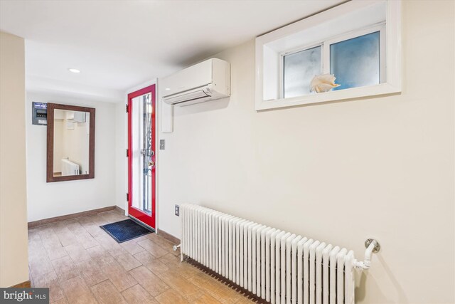 foyer entrance featuring radiator, baseboards, light wood-style floors, and a wall unit AC