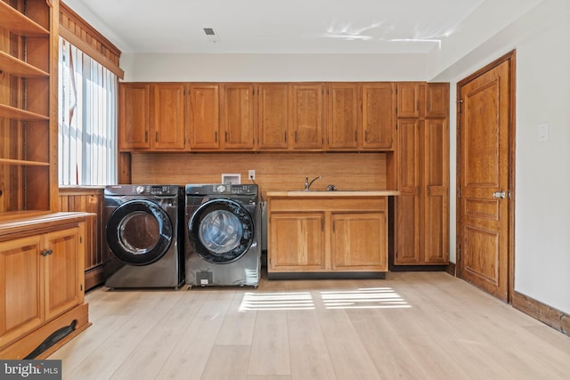 laundry area with a sink, cabinet space, washer and dryer, and light wood finished floors