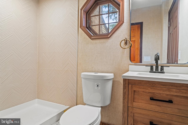 bathroom with toilet, tiled shower, and vanity