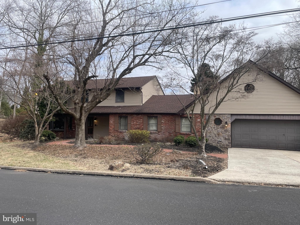 traditional-style home featuring driveway, roof with shingles, a garage, brick siding, and a chimney