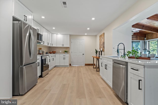 kitchen with stainless steel appliances, decorative backsplash, a sink, light wood-style floors, and visible vents
