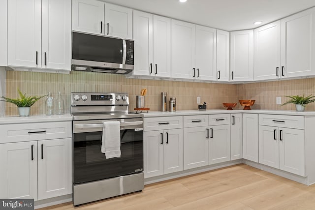 kitchen featuring light countertops, backsplash, light wood finished floors, white cabinets, and appliances with stainless steel finishes