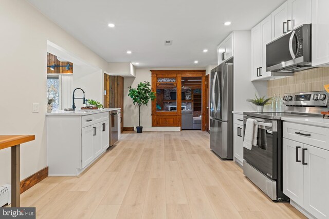 kitchen with light countertops, backsplash, a sink, light wood-style flooring, and appliances with stainless steel finishes