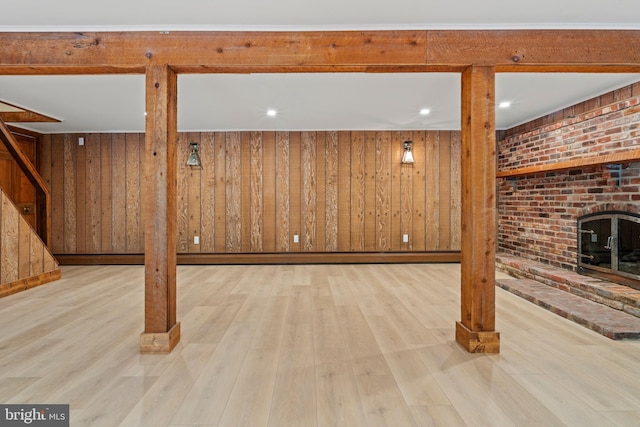 finished below grade area featuring stairs, wood finished floors, wood walls, and a brick fireplace