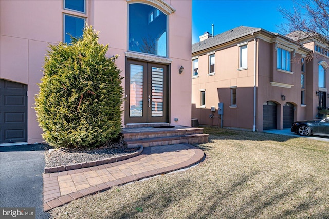 property entrance featuring stucco siding, driveway, french doors, a yard, and a garage