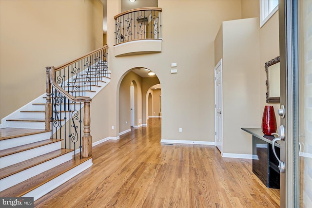 foyer entrance featuring baseboards, arched walkways, a high ceiling, and wood finished floors