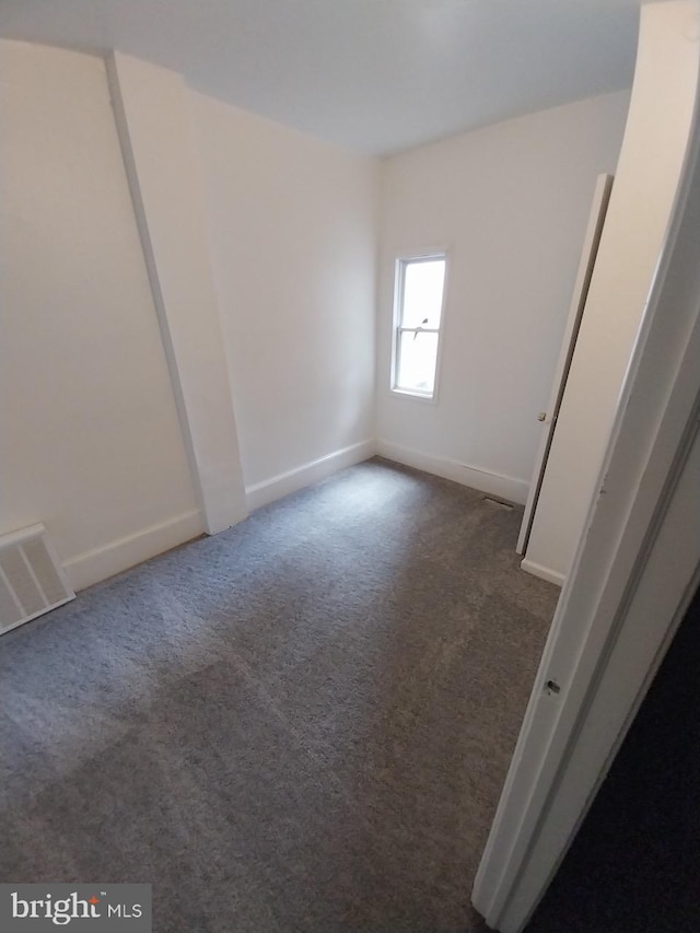 spare room with baseboards, visible vents, and dark carpet