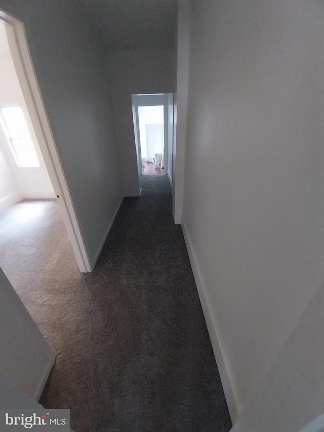 hall with baseboards and dark carpet