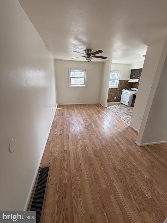 unfurnished living room with a ceiling fan, wood finished floors, visible vents, and baseboards