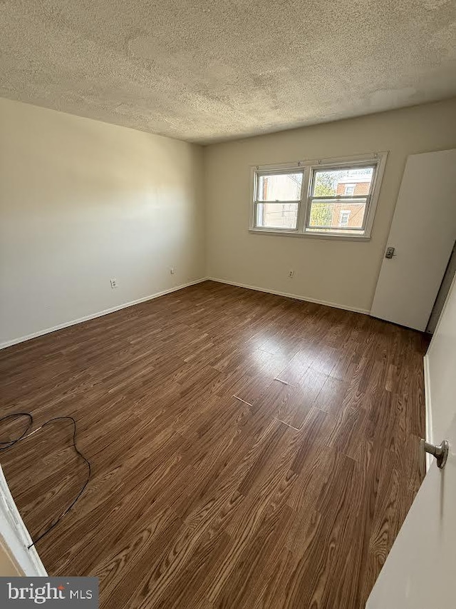 spare room with baseboards, dark wood-style flooring, and a textured ceiling