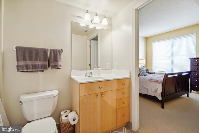 ensuite bathroom with connected bathroom, toilet, visible vents, and vanity