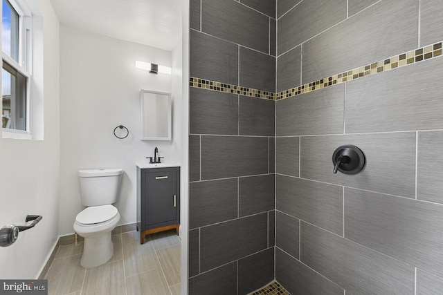 bathroom with baseboards, toilet, vanity, and a tile shower