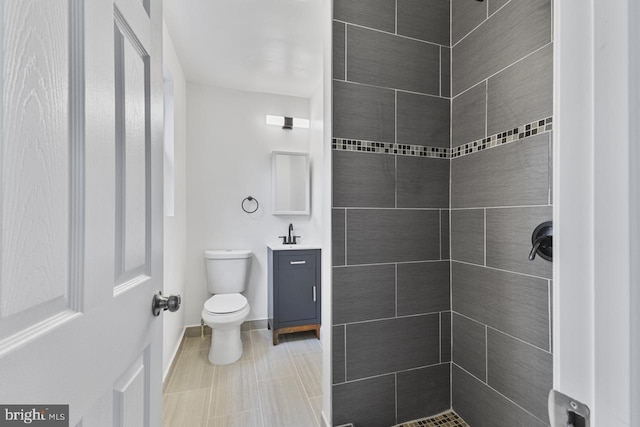 full bath featuring vanity, toilet, baseboards, and a tile shower