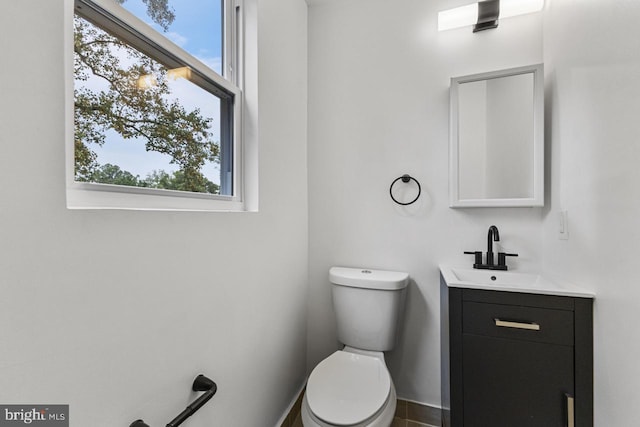 bathroom with a healthy amount of sunlight, toilet, vanity, and baseboards