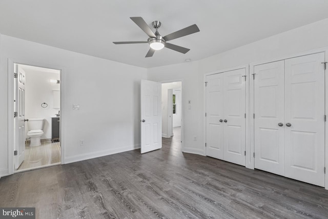 unfurnished bedroom featuring wood finished floors, multiple closets, ensuite bathroom, and baseboards