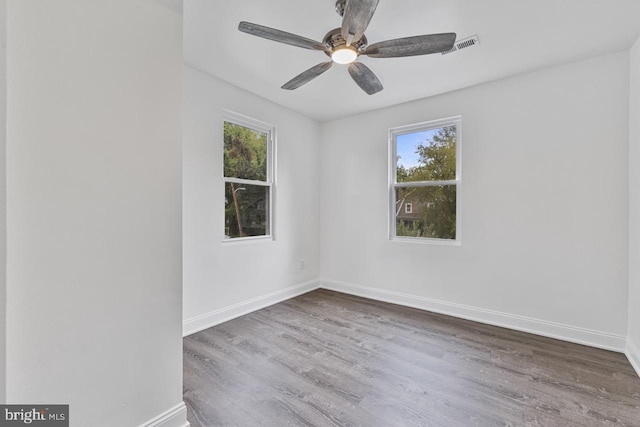 empty room featuring a wealth of natural light, baseboards, wood finished floors, and ceiling fan