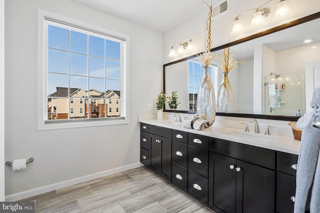 full bathroom featuring double vanity, walk in shower, baseboards, and a sink