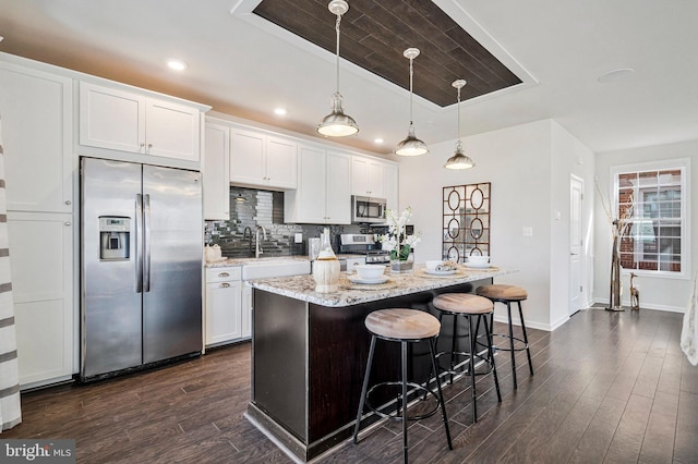 kitchen with a breakfast bar area, decorative backsplash, stainless steel appliances, dark wood-style floors, and white cabinetry