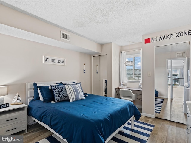 bedroom featuring baseboards, visible vents, wood finished floors, and a textured ceiling