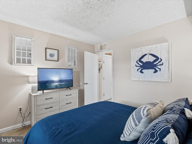 bedroom featuring wood finished floors, a textured ceiling, baseboards, and visible vents