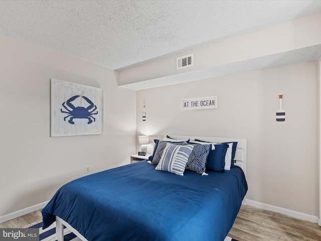bedroom with wood finished floors, a textured ceiling, baseboards, and visible vents