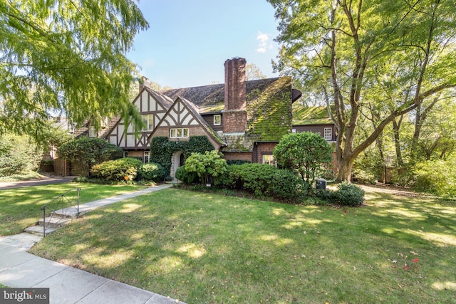 tudor-style house with stucco siding, brick siding, a chimney, and a front yard