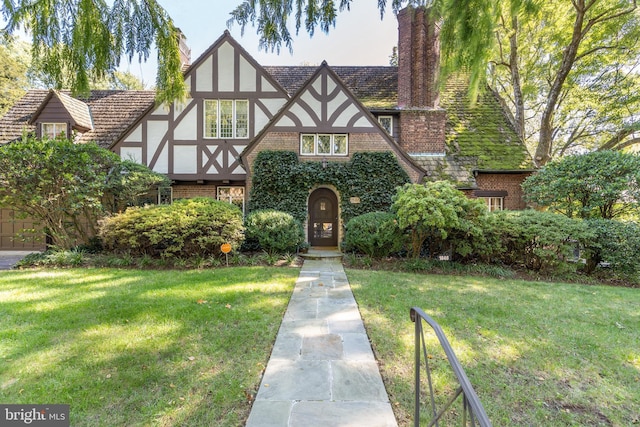 tudor house featuring stucco siding, brick siding, a chimney, and a front lawn