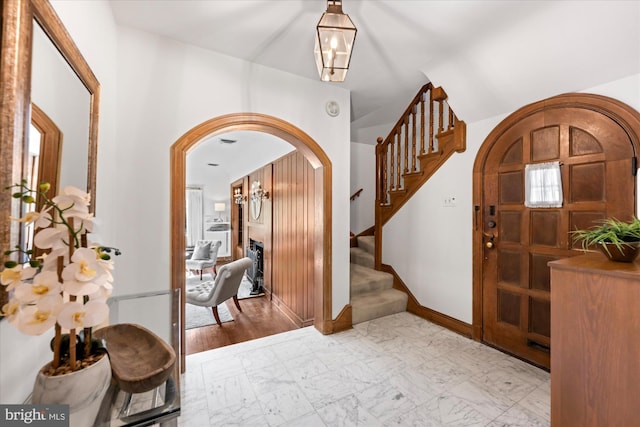 foyer featuring arched walkways, stairway, marble finish floor, and baseboards