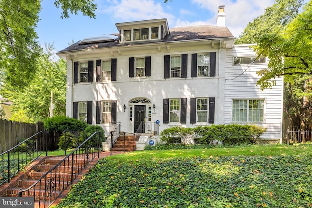 view of front of house with a front lawn, brick siding, a chimney, and fence