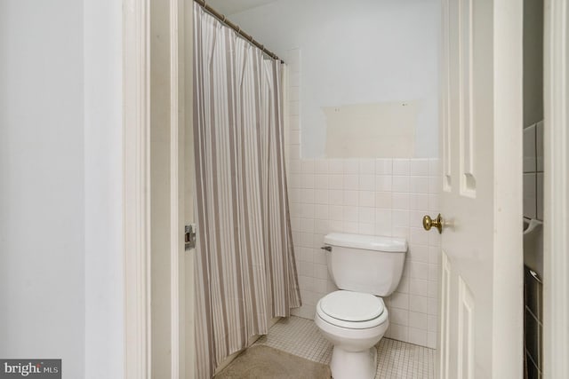 bathroom with toilet, curtained shower, tile walls, wainscoting, and tile patterned flooring