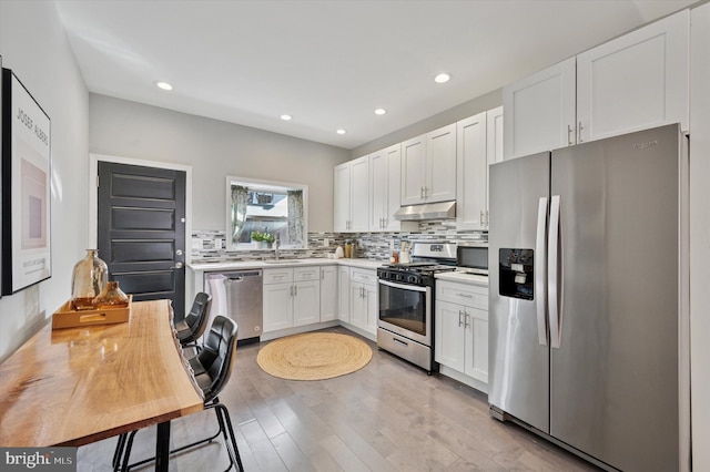 kitchen with tasteful backsplash, under cabinet range hood, light countertops, stainless steel appliances, and white cabinetry