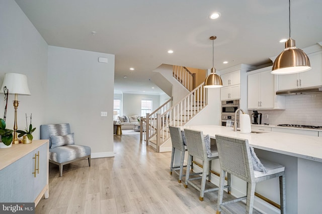 kitchen featuring tasteful backsplash, light wood-style flooring, white cabinetry, gas cooktop, and a sink