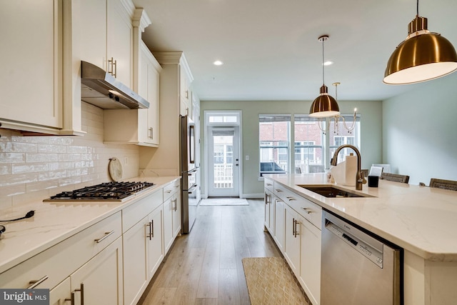 kitchen with under cabinet range hood, a sink, backsplash, appliances with stainless steel finishes, and light wood finished floors