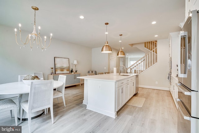 kitchen featuring an island with sink, a sink, light wood-style floors, appliances with stainless steel finishes, and white cabinetry