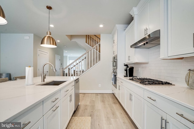 kitchen featuring light wood-style flooring, stainless steel appliances, a sink, white cabinets, and under cabinet range hood