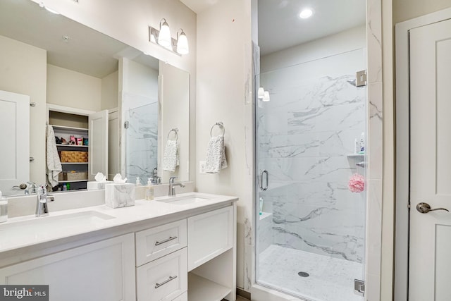 bathroom with a marble finish shower, double vanity, a walk in closet, and a sink