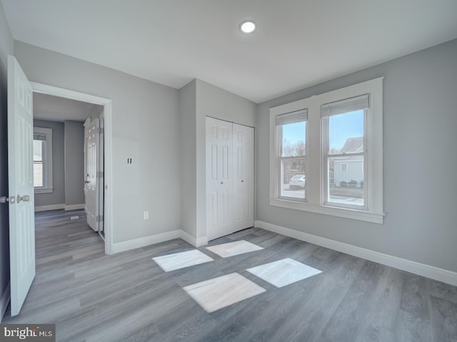 unfurnished bedroom featuring light wood-style flooring, multiple windows, baseboards, and a closet