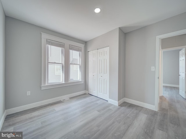 unfurnished bedroom with visible vents, wood finished floors, a closet, baseboards, and attic access