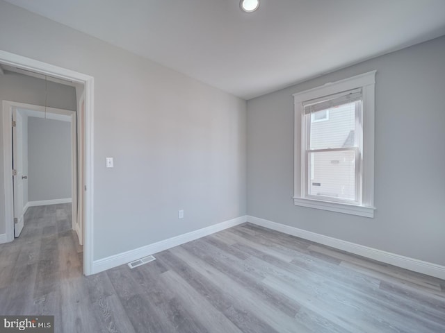 spare room featuring visible vents, attic access, baseboards, and wood finished floors